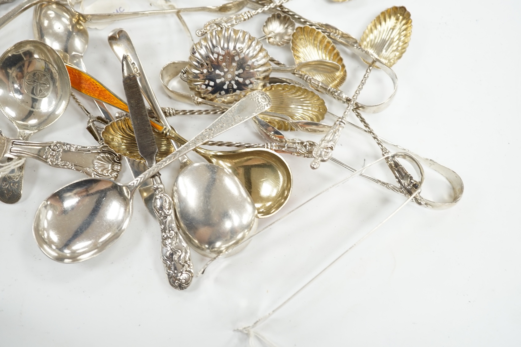 A collection of assorted small silver, sterling and white metal flatware, including two 19th century caddy spoons, enamelled spoon, sifter spoon, teaspoons, sugar tongs, etc. 9oz and two nail implements. Condition - poor